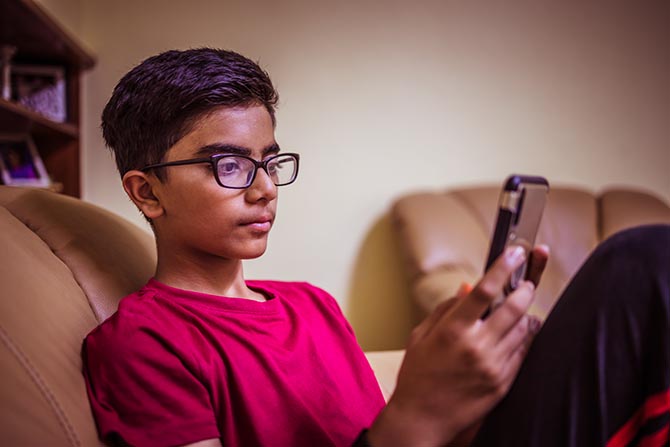 Young person sitting on a couch holding up a phone